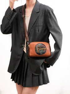 Detailed close-up of brown leather crossbody bag with vintage elephant relief on suit