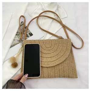 Detail showing the size of the woven envelope bag with poms and a mobile phone comparison