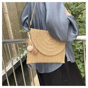 Macro detail of straw envelope crossbody bag with decorative pompoms and curved flap