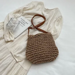 Sac en paille tressée marron posé sur une robe blanche avec bandoulière pour vacances à la plage