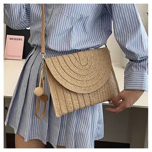 Detail of straw envelope crossbody bag featuring woven texture and decorative pom-pom