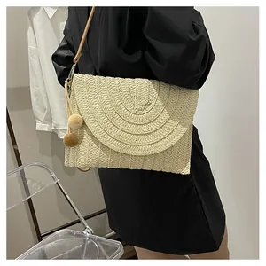 Detail of woven straw envelope bag with soft pompom charms and thin brown shoulder strap