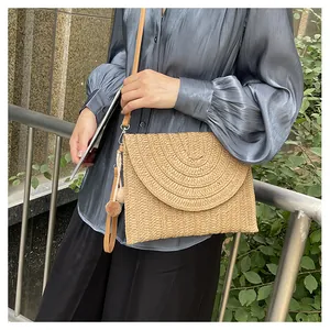 Close-up of woven straw envelope bag featuring decorative pom-pom and slim leather strap
