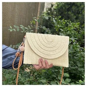 Detailed close-up of a woven envelope clutch with plush pom-poms and a PU wrist strap