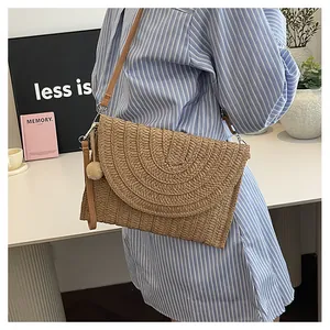 Detail of woven straw envelope bag with decorative pom pom and brown leather strap