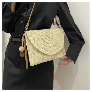 Detail of cream woven envelope bag with fuzzy pompom and slim brown shoulder strap