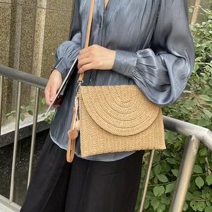 Woven straw envelope crossbody bag with pompom charms and adjustable leather strap