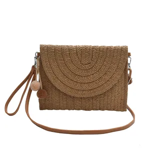 Straw woven envelope crossbody bag with pompom decor and brown leather shoulder strap