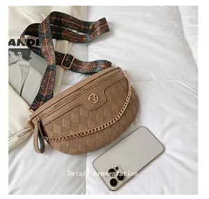 Khakifarbene Stepptasche mit goldener Kette und geblümtem Gurt neben einem Smartphone