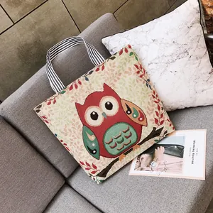 Dettaglio del ricamo a gufo su borsa tote in tela beige con manici a righe neri