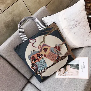 Dettaglio borsa tote in tela blu navy con ricamo a forma di gufi e manici a righe