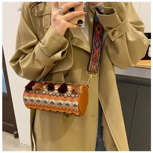 Detail of woven cylinder bag featuring bohemian tassel accents and wide embroidery strap