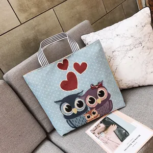 Borsa tote in tela blu con ricamo a gufo e manici a strisce su un divano grigio