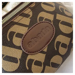 Detail of monogrammed brown leather bag featuring an embossed brand logo and gold zipper