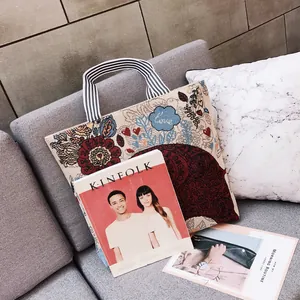Dettaglio borsa tote in tela vintage con ricamo floreale e manici a righe posata sul divano