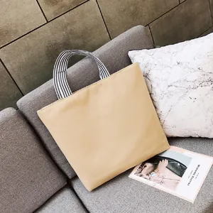 Grande borsa tote gialla in tela con manici a righe bianche e nere sul divano