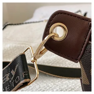 Close-up of golden swivel hook and leather detail on a brown monogram crossbody bag