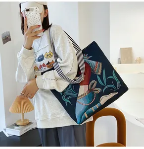 Dettaglio del ricamo artistico e della tracolla a righe sulla borsa tote in tela