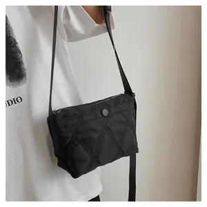 Detail of black quilted crossbody bag with rhombic stitching on a model's shoulder