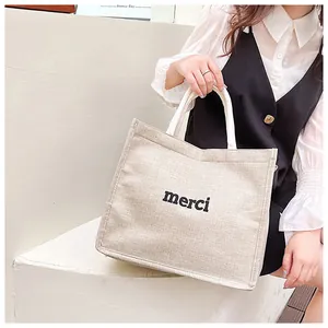 Close-up of beige linen tote bag with black merci print and white handle detail