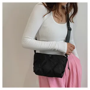 Detail of a black quilted crossbody bag with adjustable strap on a female model
