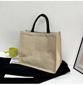 Detail view of beige canvas tote bag with black woven handles on a minimalist background