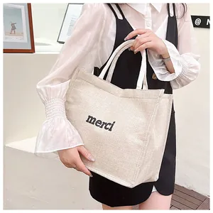 Minimalist beige linen tote bag with black merci embroidery for daily commuting