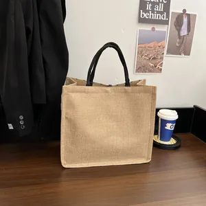 Close-up of a structured natural jute tote bag with black handles on a minimalist table