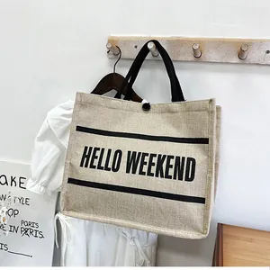 Close-up of Hello Weekend printed linen tote bag with black fabric handles and button closure