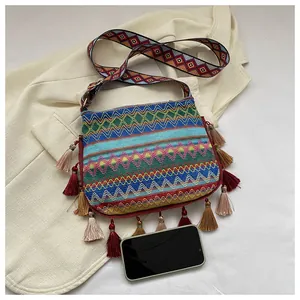 Ethnic woven crossbody bag with colorful tassels and wide strap next to a smartphone