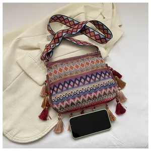 Ethnic crossbody bag with tassels and wide strap next to a phone for size scale