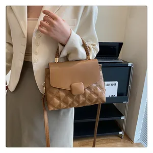 Detail view of woven top handle and diamond quilted stitching on brown handbag