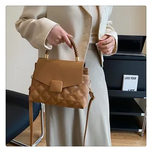 Detail of woven handle and quilted pattern on a brown crossbody bag with metal buckle