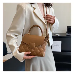 Close-up of brown quilted bag with woven handle and square buckle detail on the flap