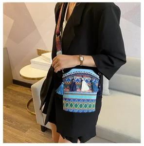 Dettaglio di borsa a secchiello intrecciata con ricamo etnico blu e nappe colorate