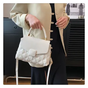 Detailed view of white quilted handbag with woven handle and gold hardware on model