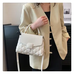Detail of white quilted handbag with woven handle and gold hardware on yellow blazer