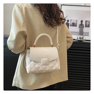 Close-up of white quilted handbag with woven handle and gold hardware on female model