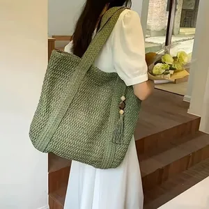Detail of green woven straw tote bag with side wooden bead tassels and shoulder strap