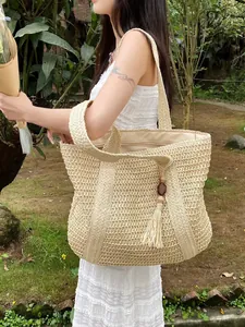 Detailed view of woven straw tote bag featuring decorative wooden beads and fringe tassel