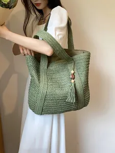 Detail of hand-woven straw tote bag in grass green with fringe and wood bead charm