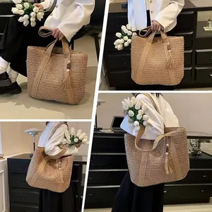 Detail of hand-woven straw tote bag featuring tassel charm and long shoulder handles
