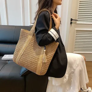 Large woven crescent straw beach tote with decorative tassels shown on a female model