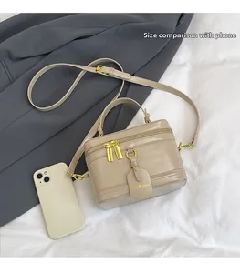 Beige Box-Umhängetasche mit goldener Hardware neben einem Handy zum Größenvergleich