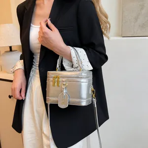 Silberne Handtasche in Boxform mit goldenen Beschlägen und Griff am schwarzen Anzug