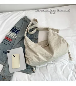 Size comparison of beige nylon dumpling bag with an iPad and phone showing large capacity