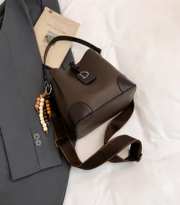 Detalle de bolso cubo marrón oscuro con hebilla en D dorada y colgante de cuentas