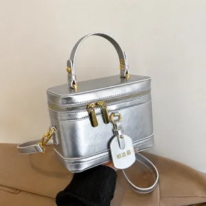 Detail der silbernen Metallic-Kosmetiktasche mit goldfarbenen Beschlägen und Griff