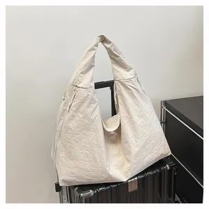 Dettaglio della borsa tote in nylon bianco sporco con tasca laterale sopra una valigia