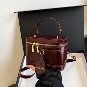 Nahaufnahme der burgunderroten Leder-Schminktasche mit goldenen Reißverschlüssen und Anhänger